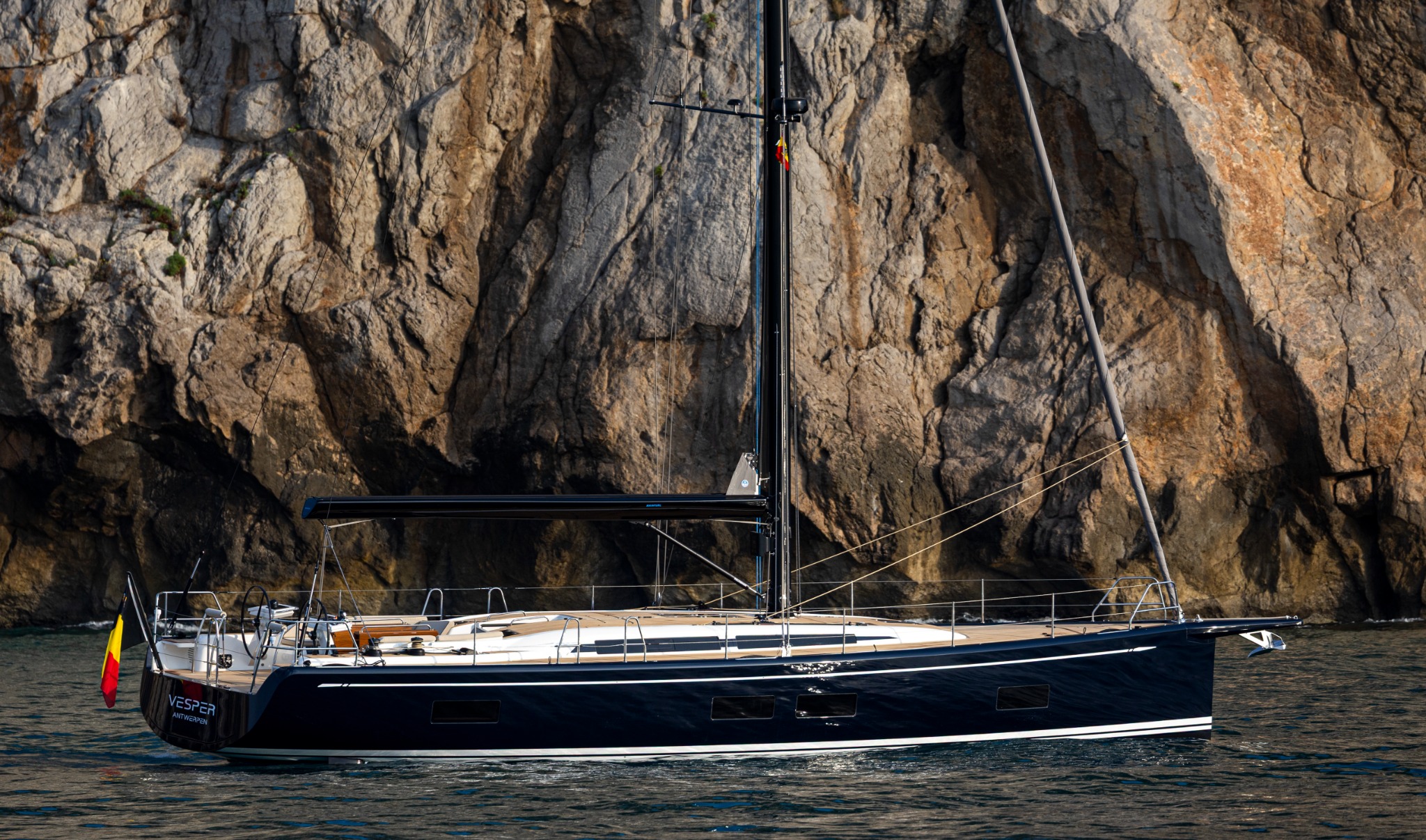 Elegant Swan 51 sailing yacht off a rocky coastline